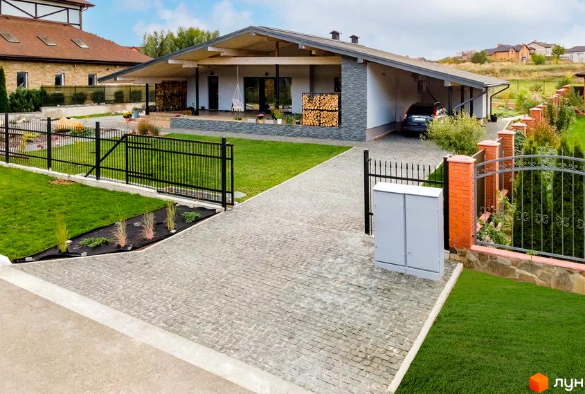 Котеджне містечко КМ Home Resort: сучасний будинок з навісом для авто та вимощеною доріжкою. Прибудинкова територія з зеленим газоном та огорожею.