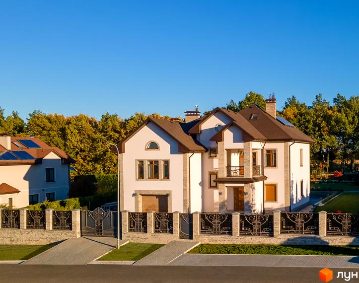 Котеджне містечко Home Resort. Білий двоповерховий будинок з коричневим дахом та кам'яними колонами. Огороджена ділянка з доглянутим газоном.