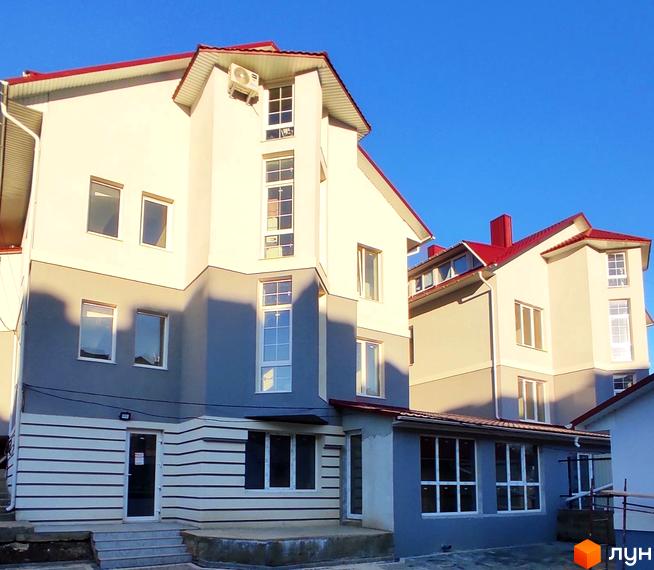 Багатоквартирний будинок з білим та сірим фасадом, червоним дахом та великими вікнами. Облаштований вхід та вимощена прибудинкова територія.