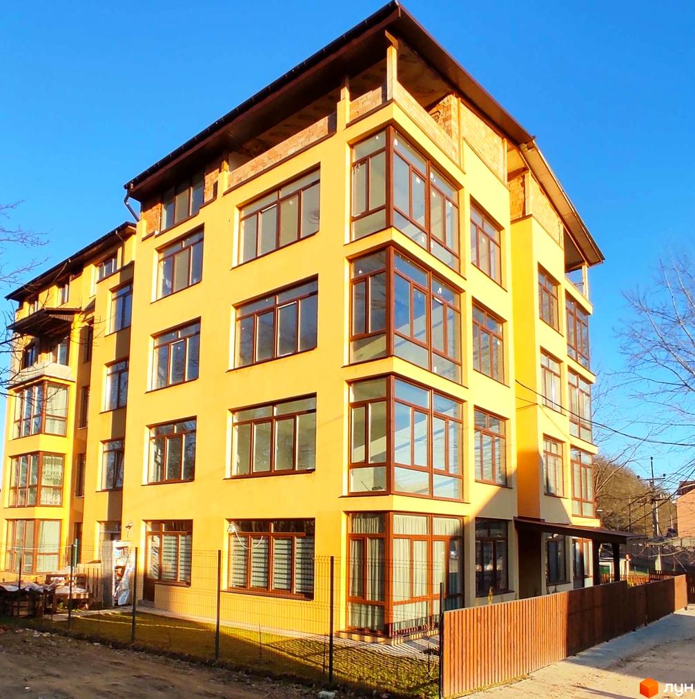 Зображення фасаду Житлового комплексу Міжнародний, жовта будівля з великими вікнами. Навколо будинку видно огорожу та зелену траву.