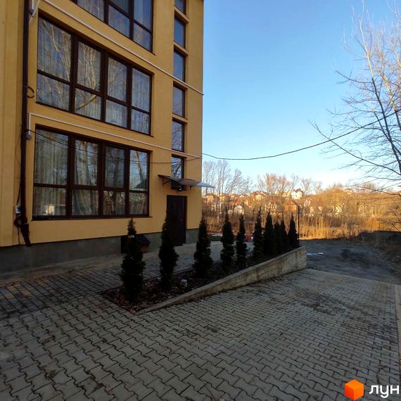 Багатоквартирний будинок Новобудови Міжнародний має світло-жовтий фасад та великі коричневі вікна. Прибудинкова територія облаштована бруківкою та рядами невеликих хвойних дерев.