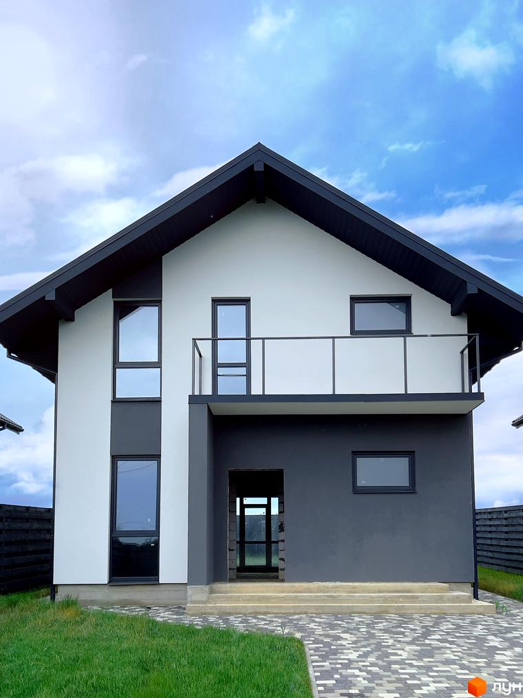 Двоповерховий будинок з темною покрівлею та великими вікнами. Перед будинком газон та бруківка, на задньому плані паркан.