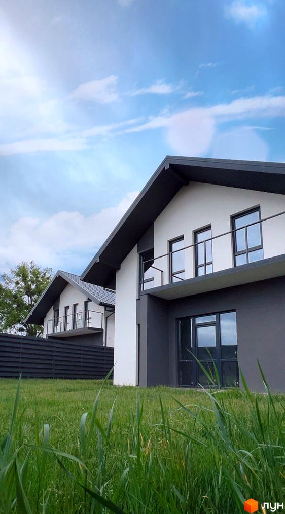 Котеджне містечко КМ Green Hill Village: двоповерхові будинки з білою та сірою обробкою, великими вікнами та балконами на тлі блакитного неба з хмарами. Зелена галявина перед будинками.