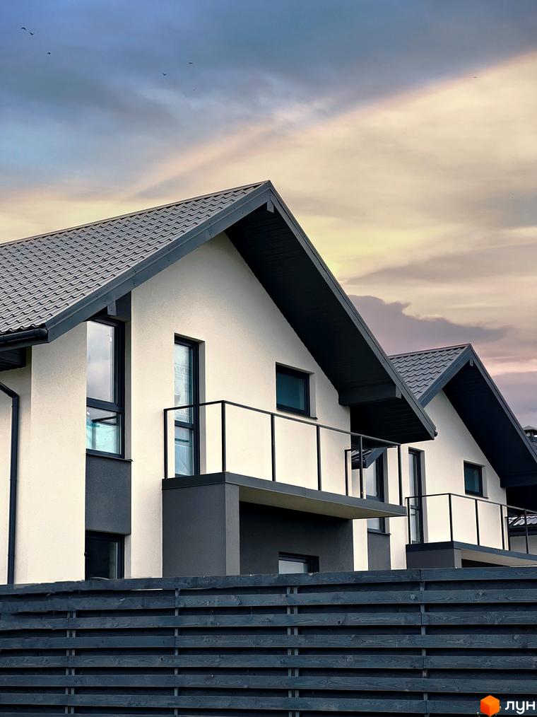 Білосніжні будинки з темною покрівлею та балконами у Котеджному містечку Green Hill Village. Дерев'яний паркан додає затишку та приватності.