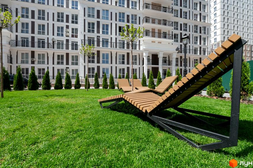 Житловий комплекс Нова Англія з білим фасадом і великими вікнами. На передньому плані зелений газон з дерев'яними лежаками.