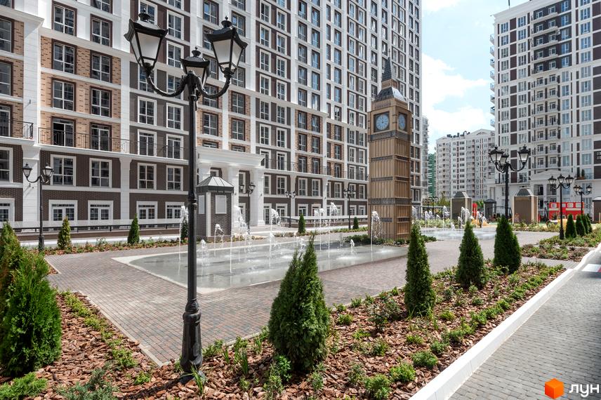 Вигляд на фасади будинків Житлового комплексу Нова Англія та прибудинкову територію з фонтаном і декоративними деревами.