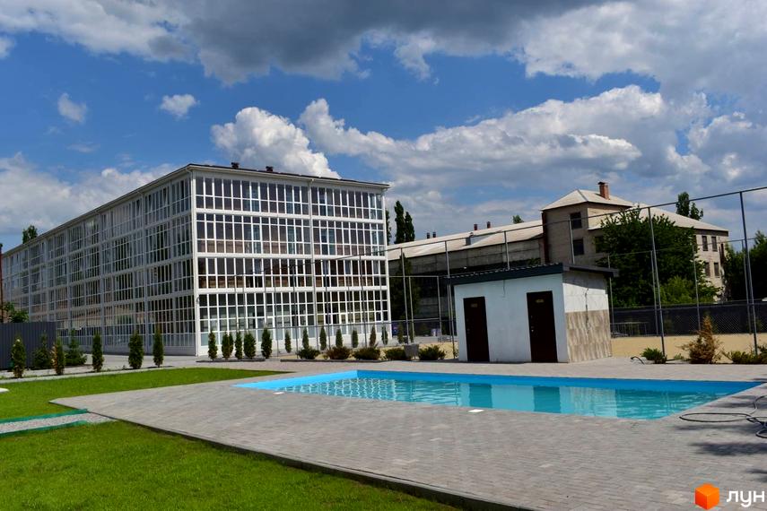 Житловий комплекс Сузір'я 2020 з великими вікнами та басейном на території. Навколо будівлі зелена зона та доглянута прибудинкова територія.
