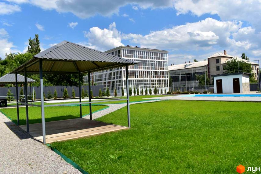 Житловий комплекс Сузір'я 2020 з білою фасадною частиною та скляними вікнами, поруч зелена галявина з альтанками та басейном.
