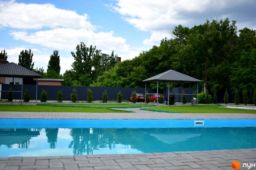 Житловий комплекс Сузір'я 2020 з басейном та зеленою зоною. На території комплексу розташовані навіси, дерева та паркан.