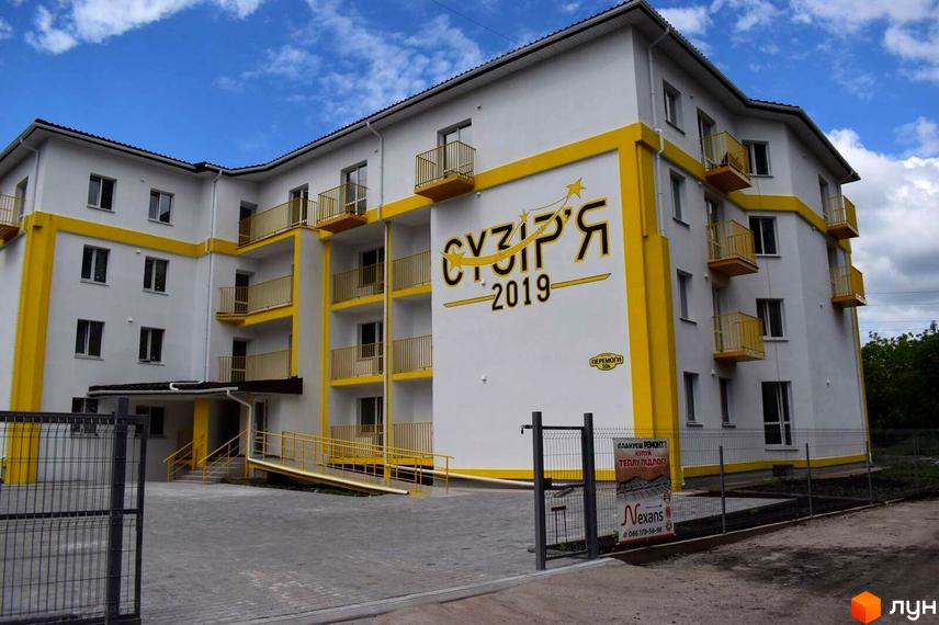 Новобудова Сузір'я 2019 з жовтими елементами та балконами, перед якою розташована прибудинкова територія з парканом.