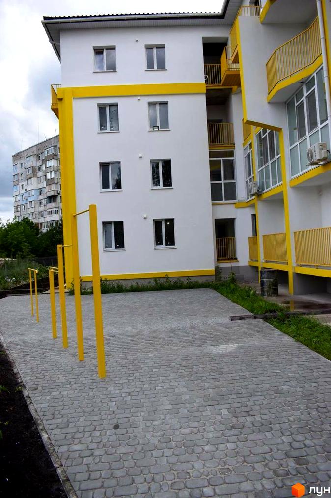 Житловий комплекс Сузір'я 2019 має біло-жовтий фасад та спортивний майданчик з жовтими турніками на бруківці.