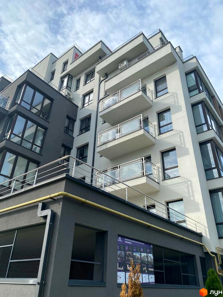 Зовнішній вигляд новобудови ЖК Бульвар Європейський. Фасад будівлі світло-сірий з темними елементами, скляними балконами та великими вікнами. На першому поверсі розташована рекламна афіша.