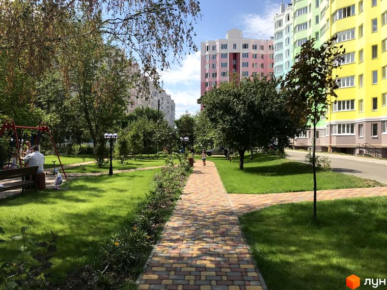 Житловий комплекс Святопетрівський: яскраві фасади будинків та зелена прибудинкова територія з доріжками та дитячим майданчиком.