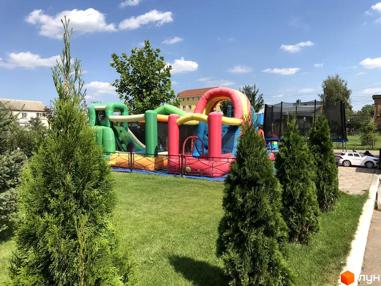 Територія Житлового комплексу Святопетрівський з яскравим надувним батутом та зеленими хвойними деревами. Зона для дитячих розваг.