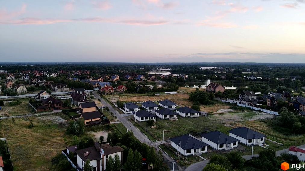 Вид на котеджі з темними дахами та білими фасадами. Навколо будівель зелена трава та дерева, створюючи атмосферу спокою та комфорту.