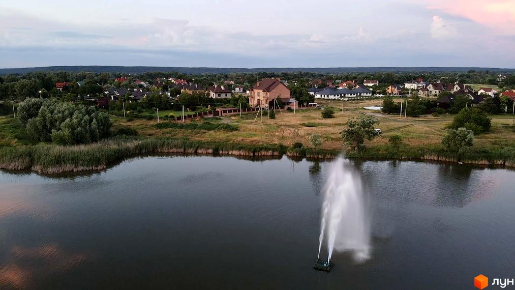 Котеджне містечко КМ Зоряний, мальовничий вид на водойму з фонтаном та зелені насадження навколо будинків.