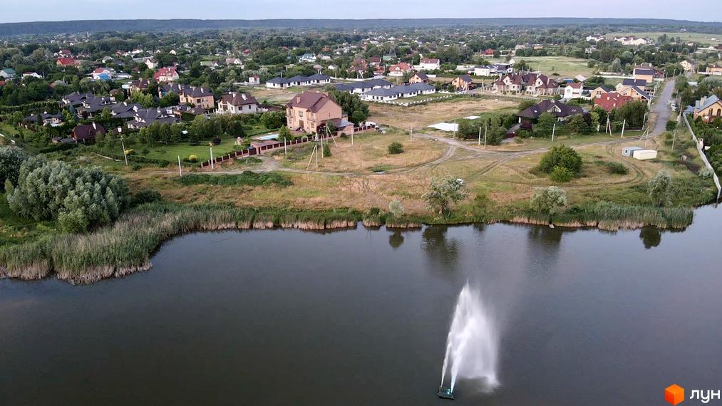 Котеджне містечко Зоряний біля озера з фонтаном, навколо зелені дерева та сучасні будинки.