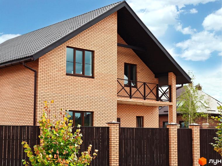 Котеджне містечко КМ Зоряний: двоповерховий будинок з цегляним фасадом та балконом. Навколо огороджена територія з деревами та парканом.