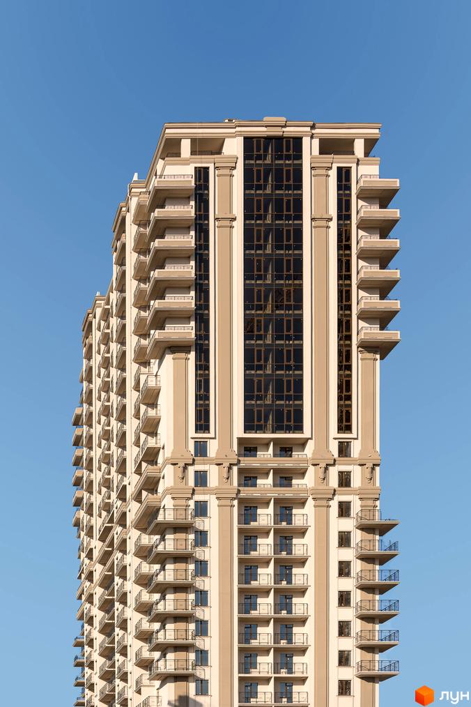 Висока будівля житлового комплексу Акрополь з балконами та великими вікнами на тлі блакитного неба.