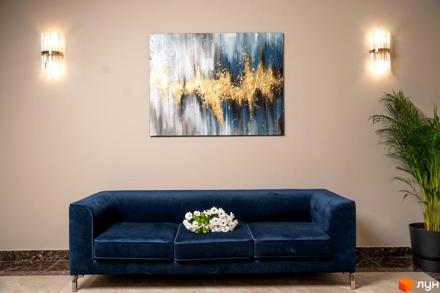 Інтер'єр кімнати з синім диваном, картиною та рослиною в Житловому комплексі Акрополь. Стіни бежевого кольору, на дивані лежать квіти.