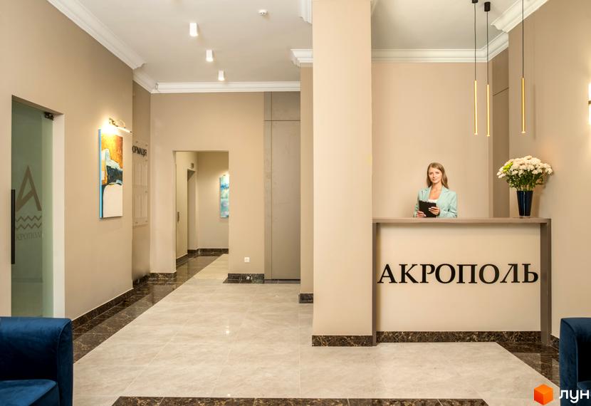 Рецепція Житлового комплексу Акрополь. Інтер'єр з дівчиною за стійкою, квітами та написом назви комплексу.