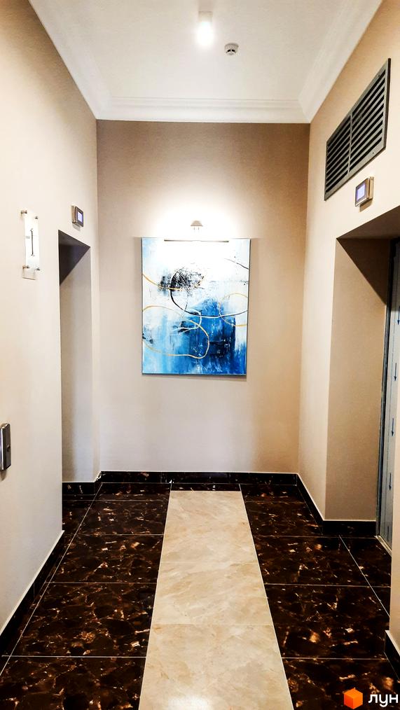 Житловий комплекс Акрополь: інтер'єрний коридор з темною плиткою під мармур та світлою центральною доріжкою. На стіні розміщена абстрактна картина.