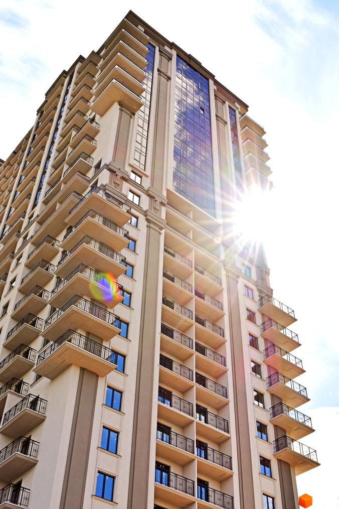 Зображення багатоповерхового будинку з балконами. Житловий комплекс Акрополь з вікнами, що відбивають сонце.