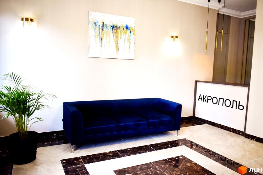 Інтер'єр холу Житлового комплексу Акрополь: просторе лобі з синім диваном, декоративною рослиною та світлими стінами.