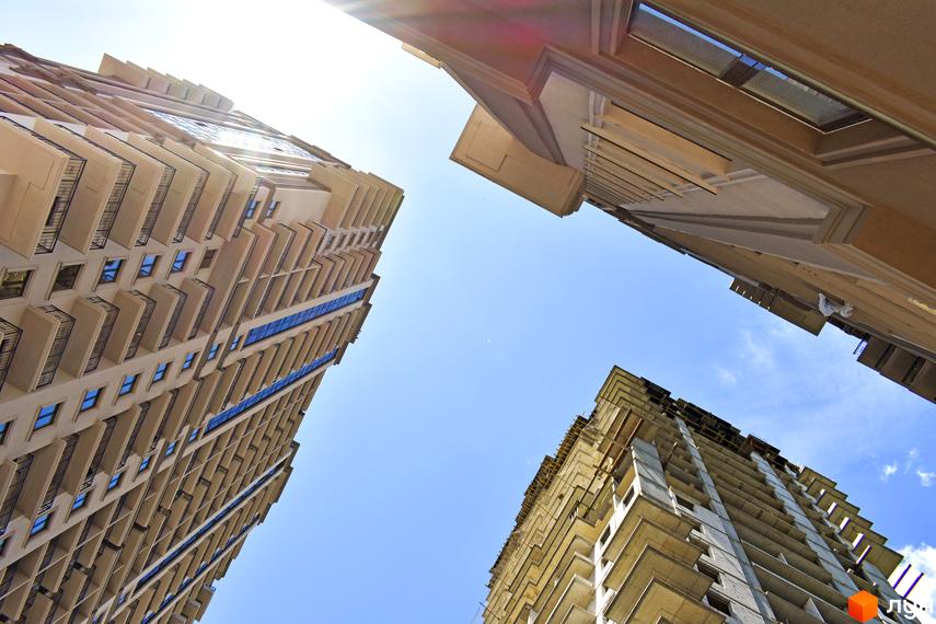 Вигляд на висотні будівлі житлового комплексу Акрополь: одна будівля завершена з балконами та синіми вікнами, інша – на етапі будівництва.