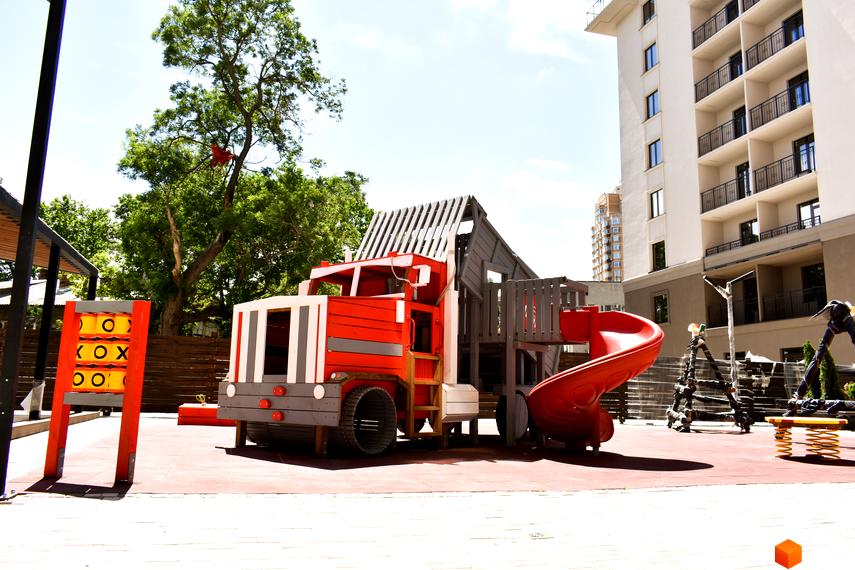 Житловий комплекс Акрополь з дитячим майданчиком у вигляді великої іграшкової вантажівки. На задньому плані багатоповерховий будинок.