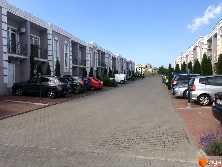 Котеджне містечко КМ Айленд: сірі будинки з білими елементами та паркуванням перед ними. Територія з бруківкою та зеленими насадженнями.