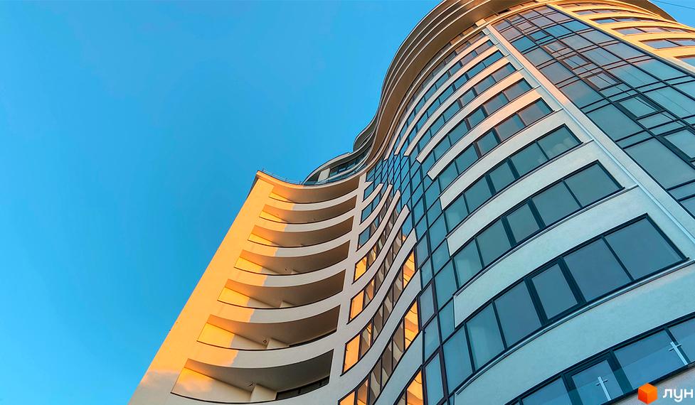 Зображення фасаду та скління Будівельного проєкту Parus з балконами. Вид знизу на багатоповерхівку та блакитне небо.