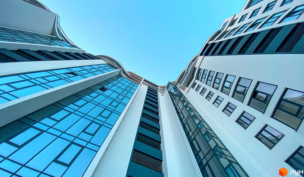 Зображення фасаду будинку Житлового комплексу Parus з великими вікнами на фоні блакитного неба. Вигляд знизу вгору.