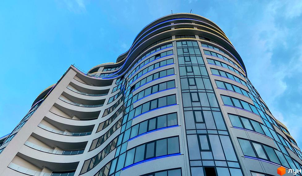 Зображення фасаду та скління багатоповерхового будинку в Житловому комплексі Parus. Вигляд будівлі знизу вгору на фоні блакитного неба.