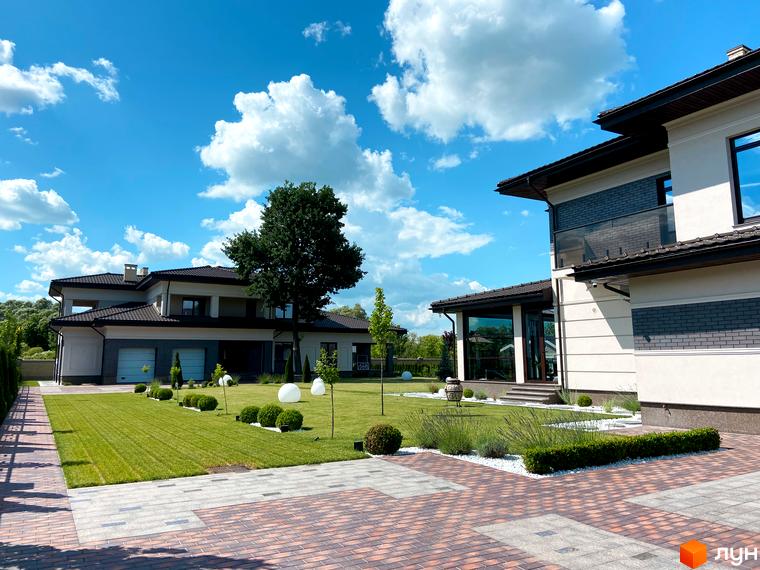 Котеджне містечко КМ Franko River Club з доглянутою прибудинковою територією та зеленим газоном. Фасад будинку виконаний у світлих тонах з елементами темної цегли.