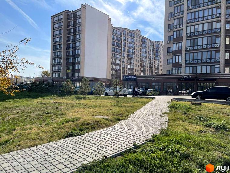 Житловий комплекс Парус: багатоповерхові будинки з комерційними приміщеннями на першому поверсі, брукована доріжка та зелений газон.