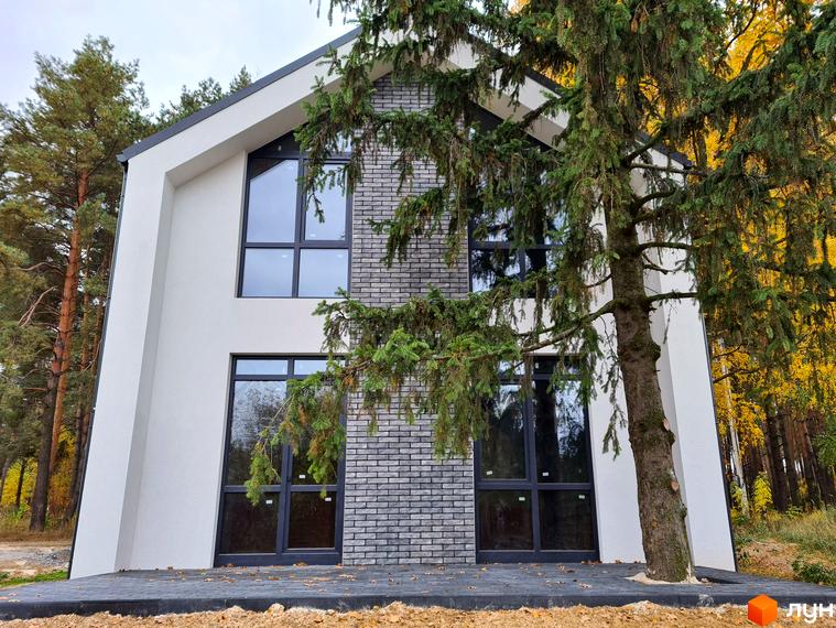 Двоповерховий будинок Котеджне містечко ForestHouse з білим фасадом, сірою цеглою та великими вікнами. Навколо будинку зелені дерева та осінній ліс.