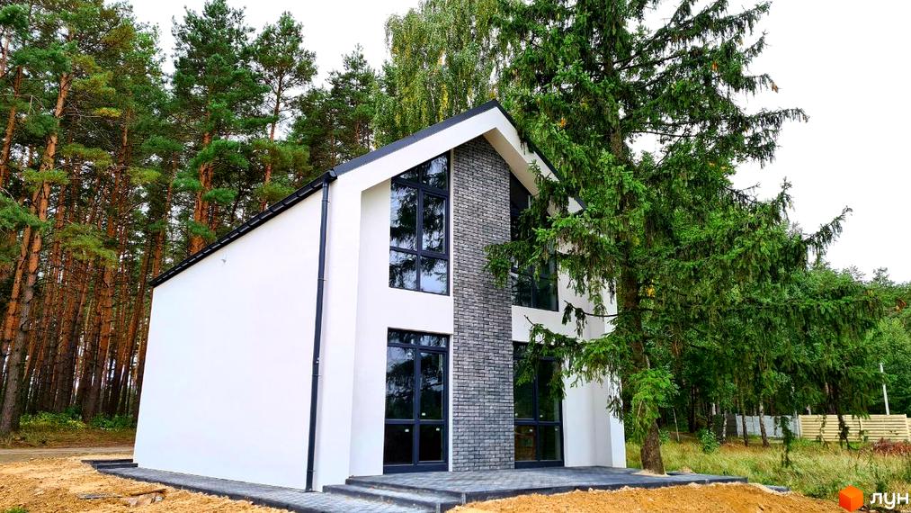 Білий двоповерховий будинок Котеджного містечка ForestHouse з темним дахом та великими вікнами, оздоблений сірою цеглою, розташований серед сосен.