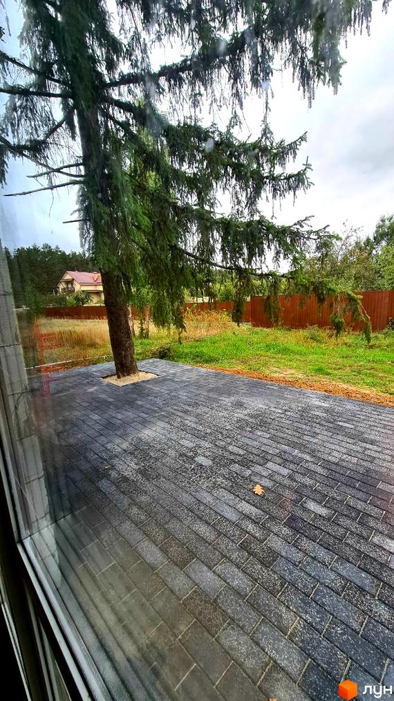 Вигляд з вікна на Котеджне містечко ForestHouse. На подвір'ї викладена плитка, росте дерево, за яким видно будинок та огорожу.