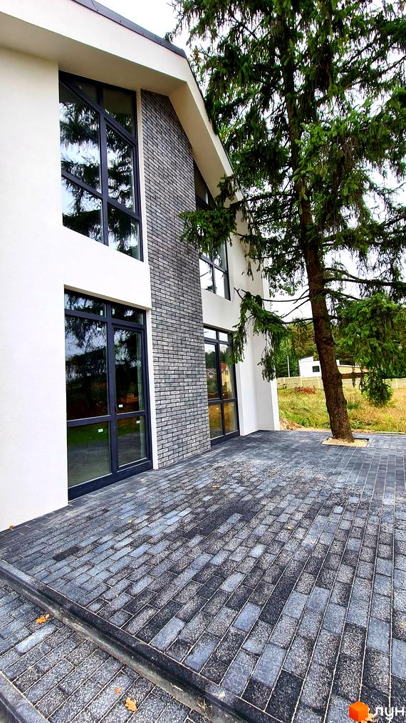 Зовнішній вигляд будинку в Котеджному містечку ForestHouse з великими вікнами та сірою цегляною кладкою. Облаштована прибудинкова територія з тротуарною плиткою.