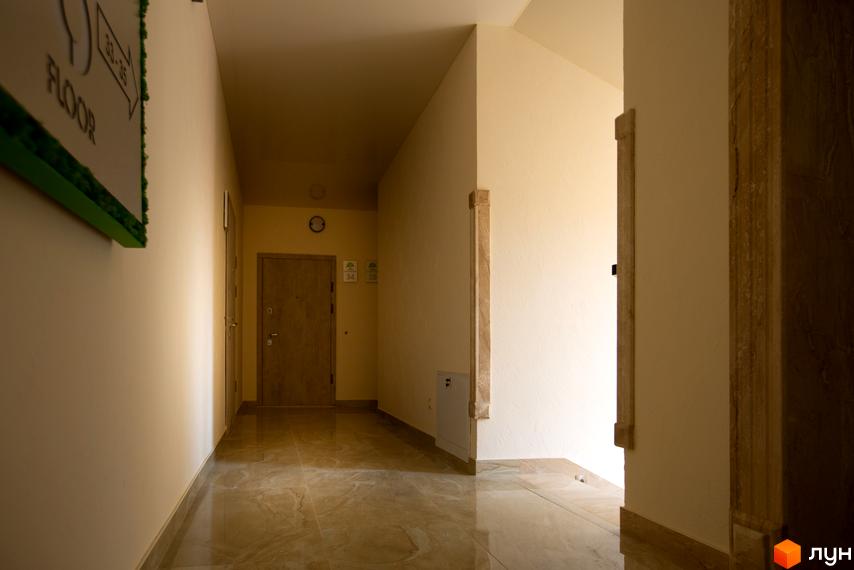 Коридор у новобудові ЖК SilverPark з дверима та вказівниками поверхів. Відкритий простір з мармуровою підлогою та світлими стінами.