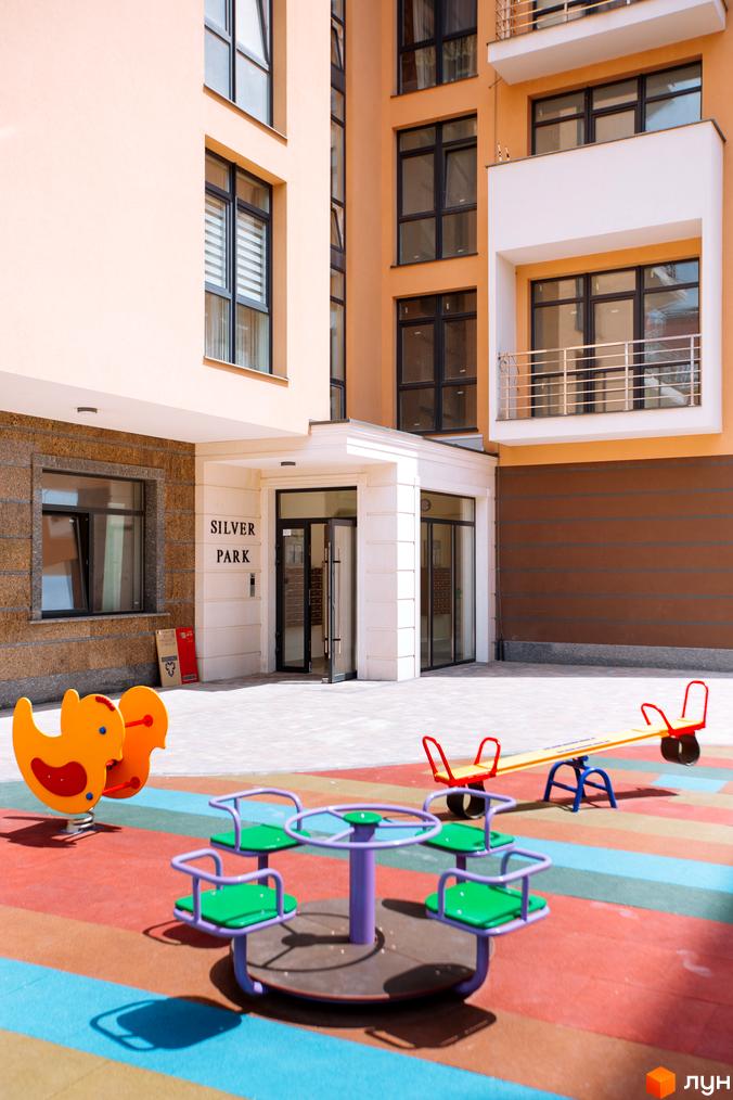 Зовнішній вигляд житлового комплексу SilverPark з дитячим майданчиком. Фасад будинку світло-бежевий, вікна темні.