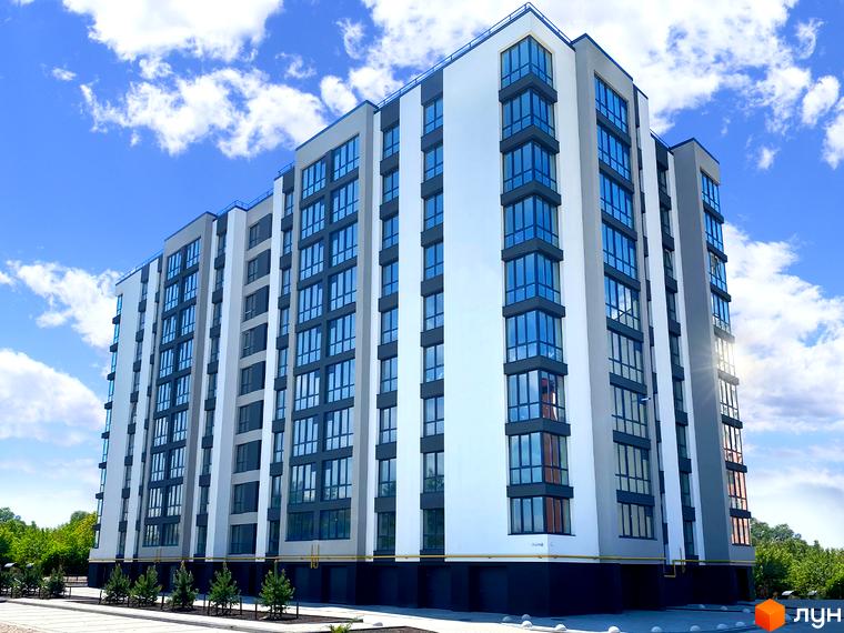 Висотна будівля ЖК Парковий з великою кількістю вікон на фоні блакитного неба з хмарами. Перед будинком розташована прибудинкова територія з деревами.