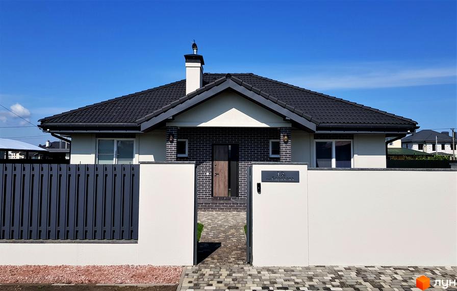 Котеджне містечко КМ Сонячний: фасад будинку з темним дахом та цегляним оздобленням, доріжка з бруківки та огорожа.