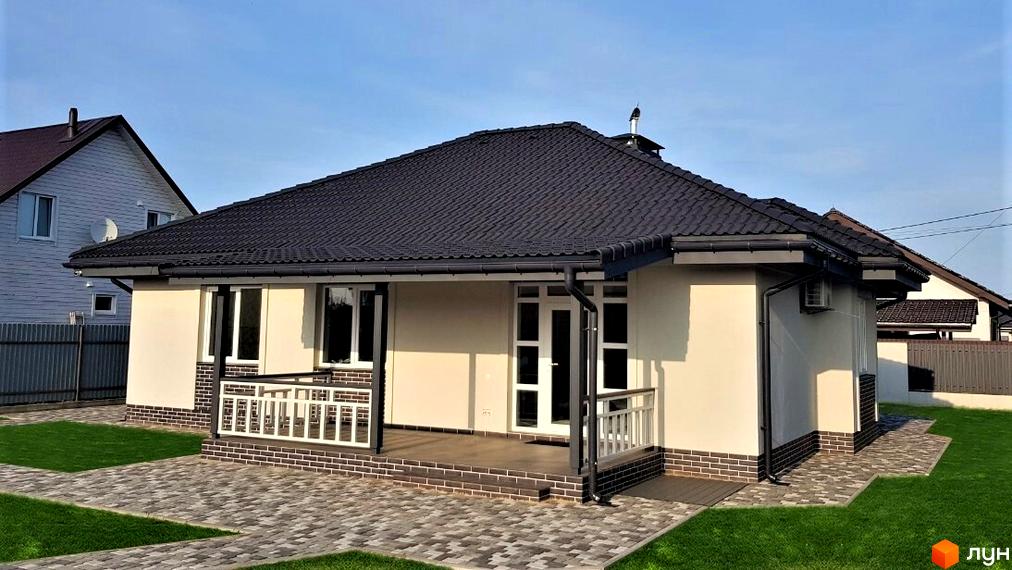 Котеджне містечко КМ Сонячний: одноповерховий будинок з темним дахом, великими вікнами та терасою. Прибудинкова територія з бруківкою та зеленою травою.