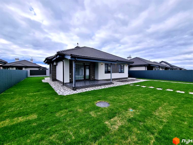 Котеджне містечко Сонячний: одноповерховий будинок з темним дахом і цегляними елементами фасаду, доглянутий зелений газон, вимощені доріжки та огороджена територія.