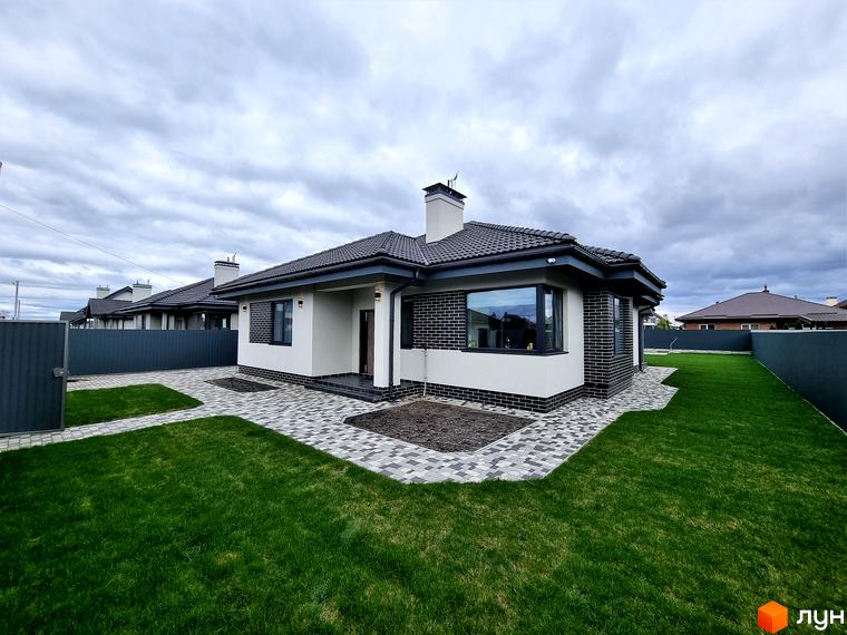 Котеджне містечко Сонячний: одноповерховий будинок з цегляним оздобленням та великим вікном. Доглянутий газон та бруківка навколо будинку.