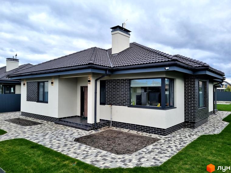 Котеджне містечко КМ Сонячний. Зовнішній вигляд будинку з білою штукатуркою, чорною цегляною обробкою та темною черепицею. Прибудинкова територія з бруківкою та зеленою травою.