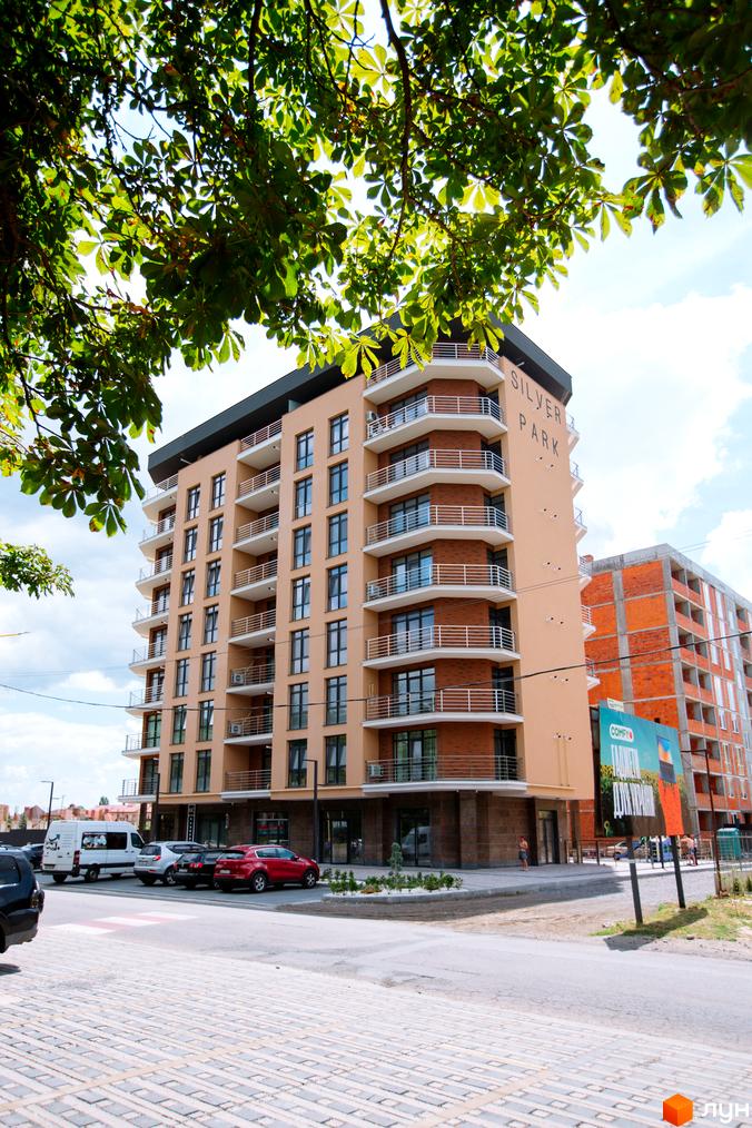 Зовнішній вигляд житлового комплексу SilverPark з балконами та вікнами. Навколо будинку розташована прибудинкова територія з автомобілями та деревами.
