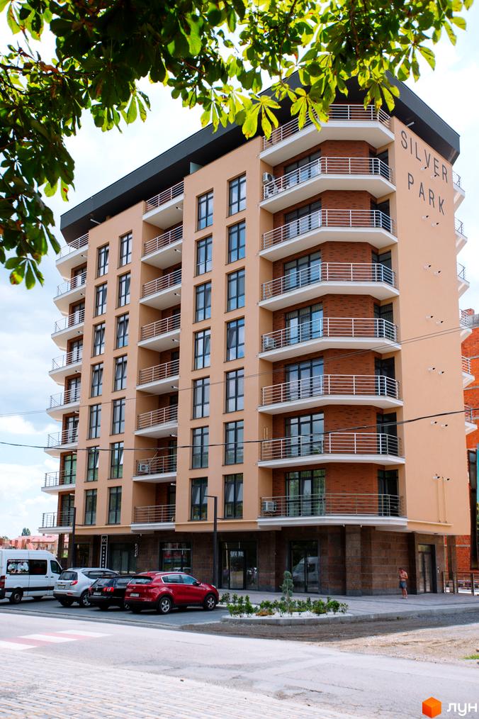 Фасад житлового комплексу SilverPark з балконами та вікнами, поруч припарковані автомобілі та білий мікроавтобус.